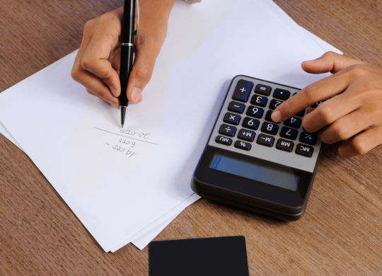 Closeup of person calculating on calculator and writing. Credit card, paper sheet and calculator lying on desk. Accountancy concept. Cropped view.
